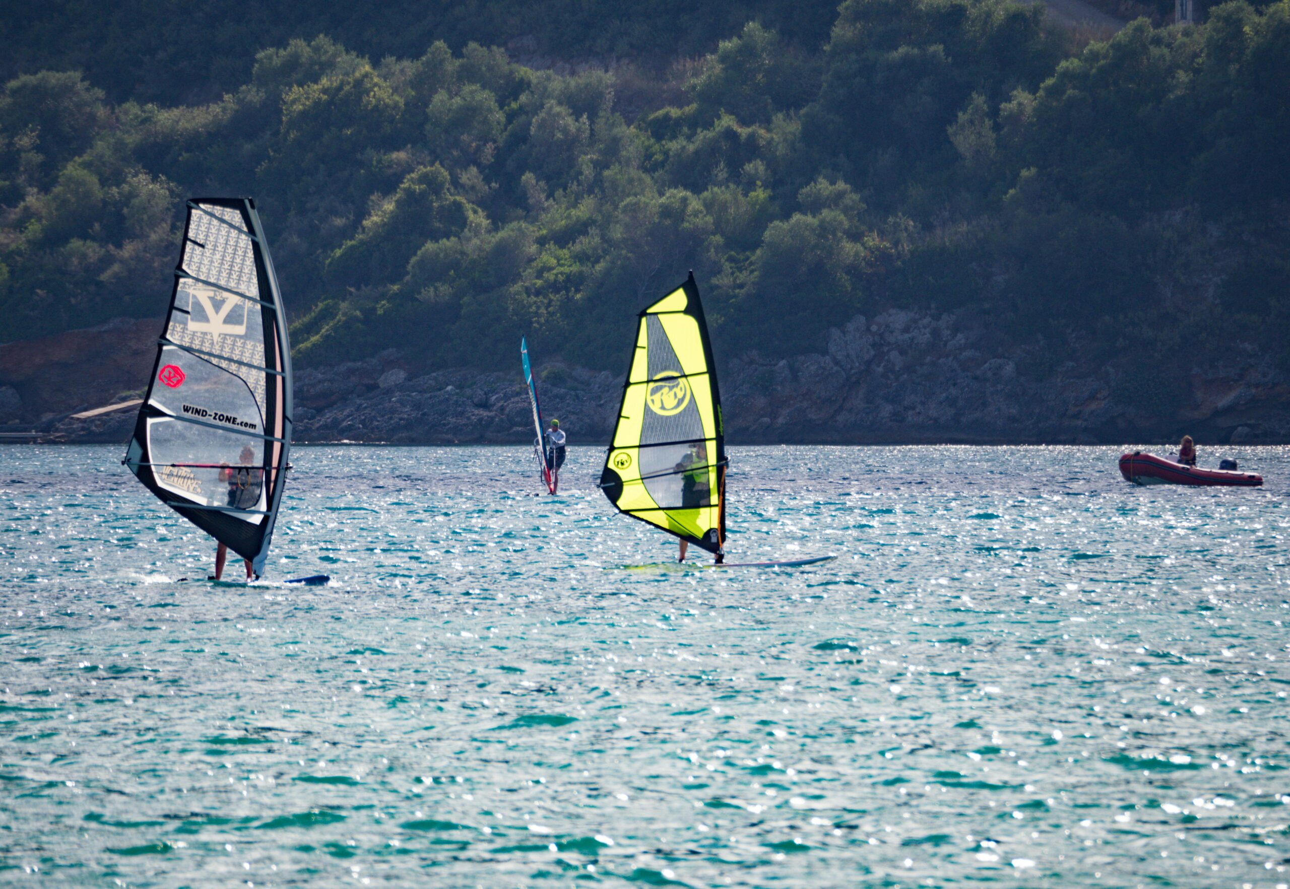 Three kitesurfers are visible on a lake with forested land in the background.  This is an example of the environment in which students would enjoy water sports in Bristol and the surrounding areas.  Photo by Brett Jordan: https://www.pexels.com/photo/gray-and-yellow-sails-1155163/