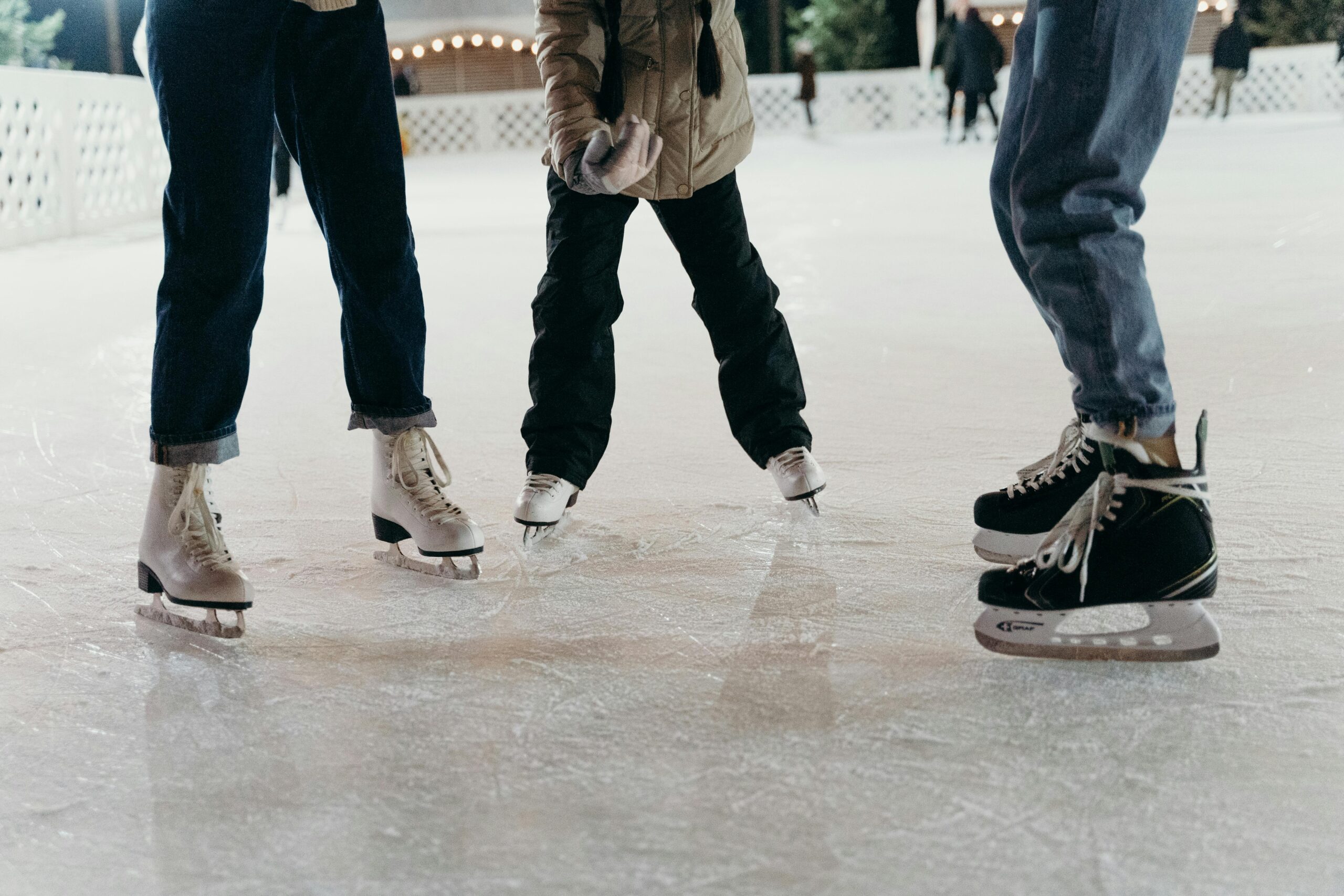 Three people's legs are visible on an ice rink, each wearing ice skates.  Their bodies and faces cannot be seen.  This is an example of how students can go ice skating in Bristol.  Photo by cottonbro studio: https://www.pexels.com/photo/people-ice-skating-together-6289768/