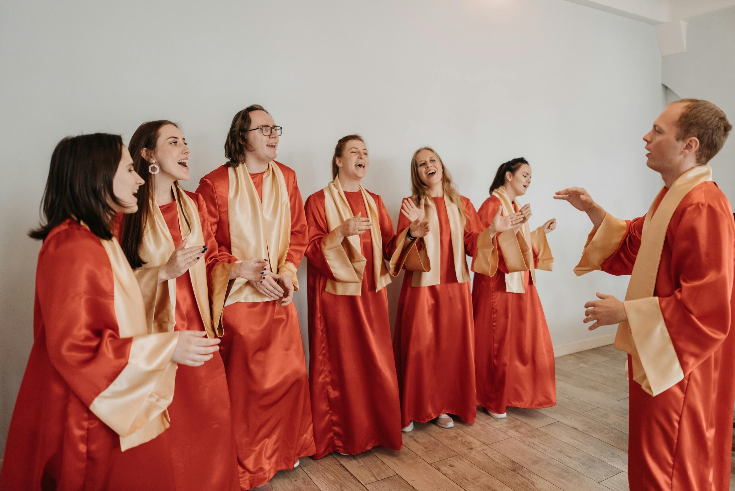 A group of singers in traditional dress sing together as one man conducts them.  This is an example of the environment students would experience in joining choirs in Bristol.  Photo by Pavel Danilyuk: https://www.pexels.com/photo/choir-in-red-gown-8815031/