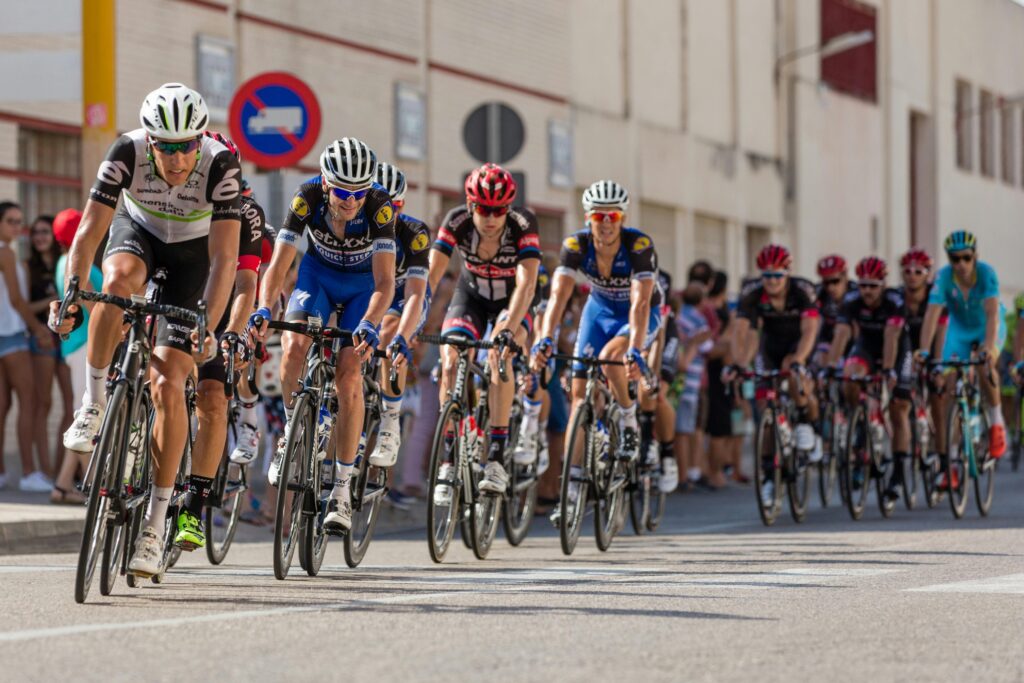 Several cyclists in helmets cycle through a town centre with buildings in the background. This is an example of how students can enjoy cycling in Bristol. Photo by Pixabay: https://www.pexels.com/photo/panoramic-view-of-people-in-bicycles-248559/